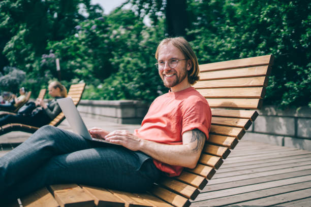 istock Man using laptop and lying on wooden bench in park 1475619028