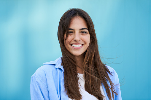 Portrait young beautiful smiling woman looking camera with sky blue background. Fashionable girl in casual attire. Positive cheerful female Caucasian people confident posing sharing on social media.