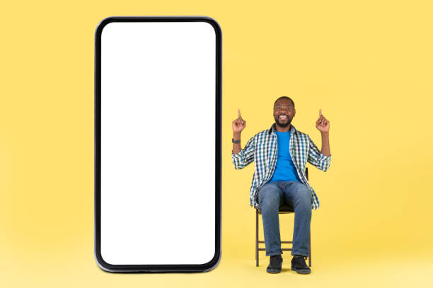 istock Black Guy Sitting Near Big Phone Pointing Fingers Up, Studio 1475624053
