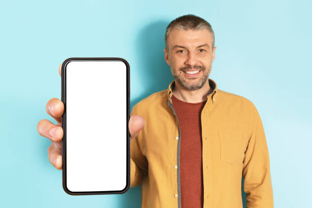 istock App advertisement. Happy mature man showing big white empty smartphone screen, recommending website or app, mock up 1475624199