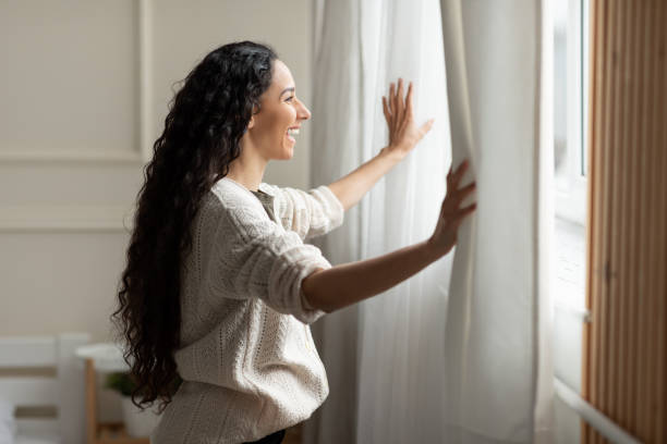 istock Excited lady opening window curtains at home 1475624237