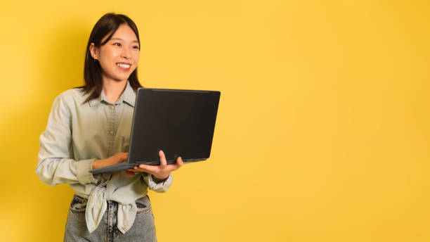 istock Young Asian woman using laptop, searching internet, working online, checking new website, looking at empty space 1475624429