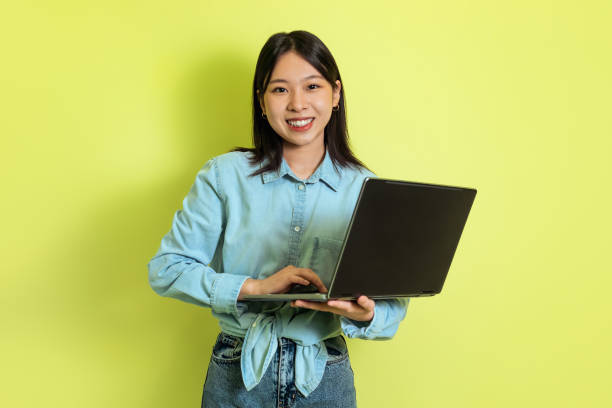 istock Korean Female Freelancer Using Laptop Computer Standing Over Yellow Background 1475624451