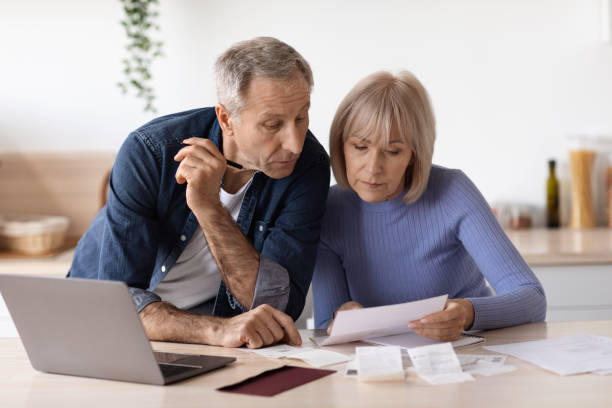 istock Elderly couple sitting at table using laptop, paying bills 1475624584