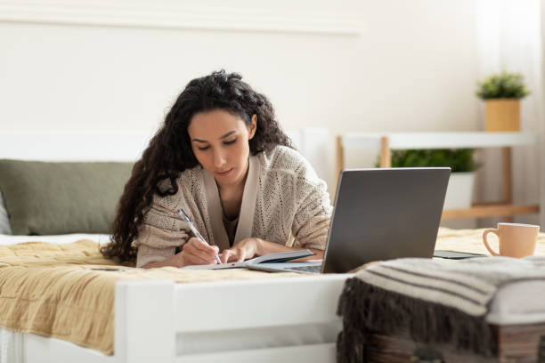 istock Focused young woman using laptop, working or studying online, taking notes during business meeting or webinar at home 1475624700