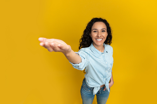 Excited young woman outstretching cupped hand, trying to hold something invisible on her palm, giving it away or asking for something, orange yellow wall, copy space, above top high angle view