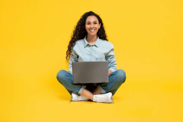 istock Happy young woman using laptop pc for online work or studies, sitting cross legged on yellow studio background 1475624895