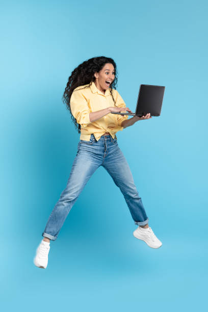 istock Excited Middle Eastern Lady Holding Laptop Jumping Over Blue Background 1475624906