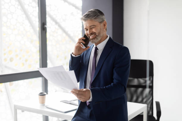 istock Smiling Middle Aged Businessman Talking On Cellphone And Checking Papers In Office 1475624977