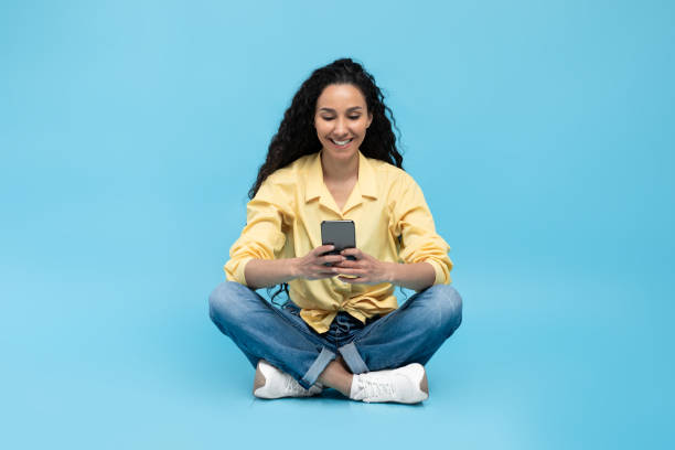istock Arabic Female Using Mobile Phone Texting Sitting Over Blue Background 1475625062