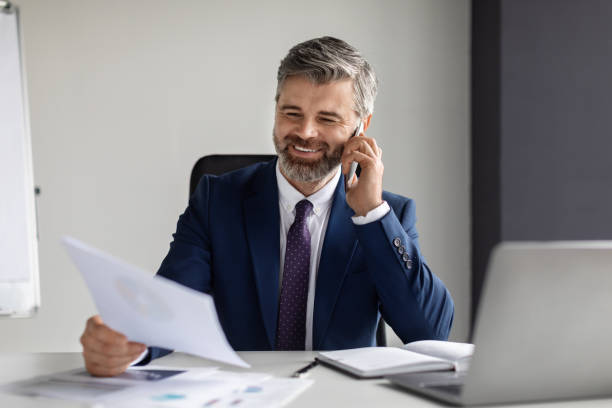 istock Smiling Middle Aged Businessman Talking On Cellphone And Checking Papers At Office 1475625218