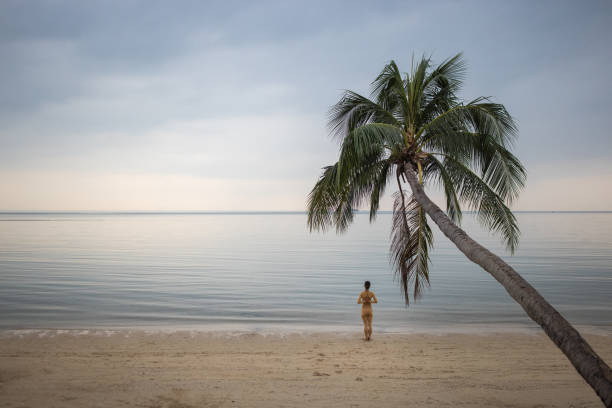 Woman exercising yoga on the beach by the calm sea in sunset alone.