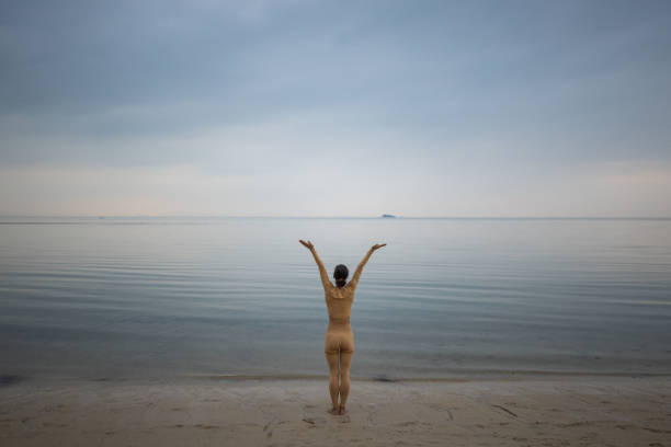 Woman exercising yoga on the beach by the calm sea in sunset alone.