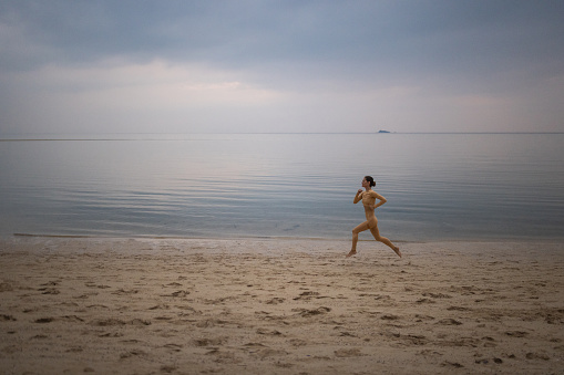 Woman jogging on the beach by the calm sea in sunset alone.