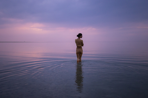 Woman standing in a shallow calm sea and enjoying a beautiful purple sky.