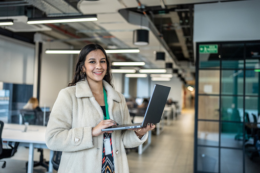 Portrait of a young woman holding laptop at office