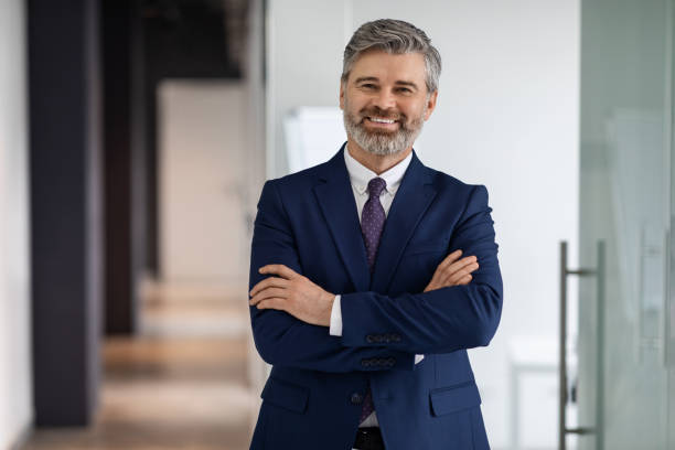 retrato del apuesto hombre de negocios de mediana edad en traje de pie con los brazos cruzados - white collar worker fotografías e imágenes de stock