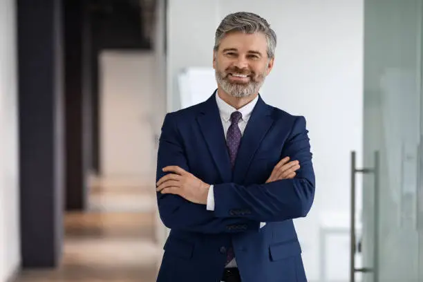 Portrait Of Confident Handsome Middle Aged Businessman In Suit Standing With Folded Arms, Successful Male Entrepreneur Posing In Office Hall, Advertising Professional Services, Smiling At Camera