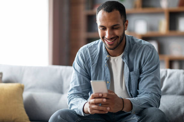 istock Handsome Young Black Man Using Smartphone While Relaxing On Couch At Home 1475634221
