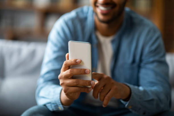 istock Closeup Shot Of Smiling Black Man Using Smartphone While Sitting On Couch 1475634230