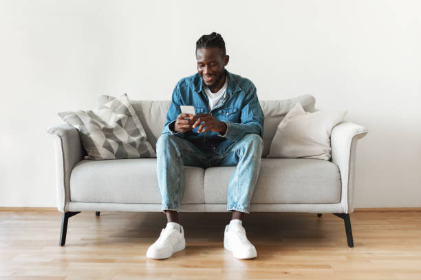 istock Black Male Using Phone Texting Sitting On Couch At Home 1475634244
