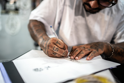 Tattoo artist's hands drawing a tattoo on the paper at a tattoo studio