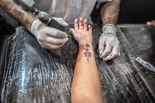 Tattoo artist's hands tattooing a woman's arm at a tattoo studio