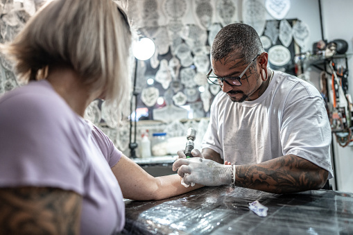 Tattoo artist tattooing a woman's arm at a tattoo studio