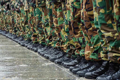 Military boots and camouflage trousers of many soldiers in uniform in a row during a training