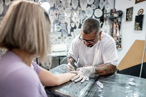 Tattoo artist tattooing a woman's arm at a tattoo studio