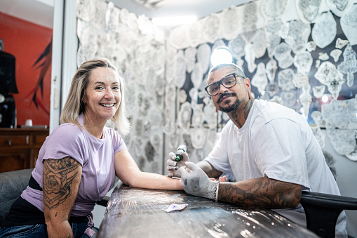 Portrait of a tattoo artist tattooing a woman's arm at a tattoo studio
