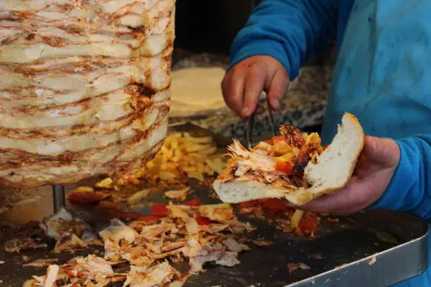 A man is cutting a sandwich with the word meat on it. Turkish chicken doner kebab
