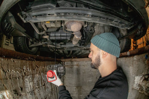 istock Young man standing in a car mechanic's pit and draining down old engine oil to a plastic holder on his own. Wide shot, fish eye lens. 1475646216