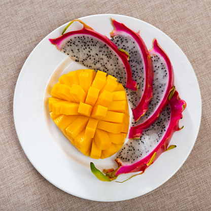 Plate of slices of ripe sweet and juicy mango and pitaya for snack. Concept of nutritional benefits of tropical fruits