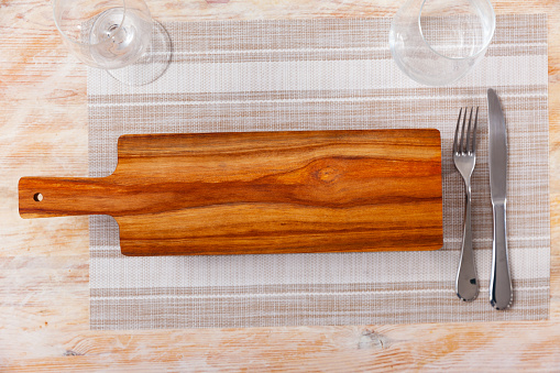 Practical wooden serving board with handle and legs on the table with other dining appliances