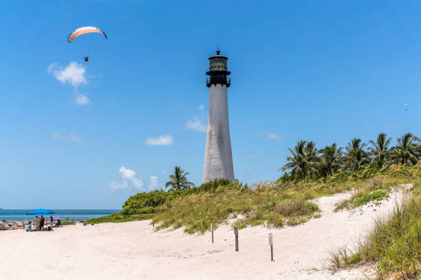 People enjoying the sea at Bill Baggs Cape Florida State Park MIAMI, FLORIDA - CIRCA JULY, 2022: People enjoying the sea at Bill Baggs Cape Florida State Park. There is parachute above the sea with people under the tent on the shore near Cape Florida Lighthouse. miami parachuting stock pictures, royalty-free photos & images
