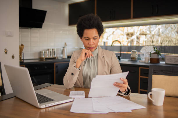 istock Mature woman using calculator while going through bills and home finances 1475666264