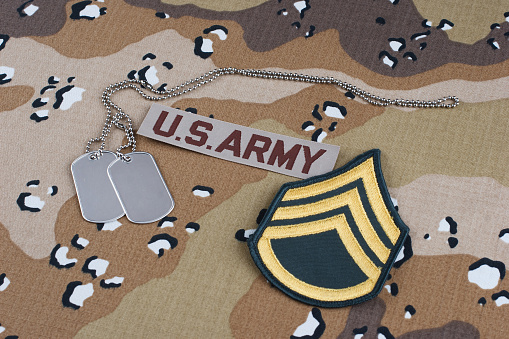 US ARMY staff sergeant rank patch and dog tags on Desert Battle Dress Uniform background