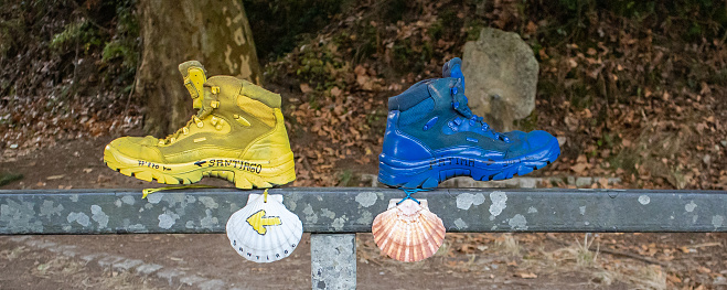 Panorama of yellow and blue boots with seashells placed on metal railing pointing in different directions in countryside