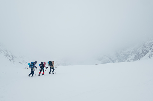 Three members rope team ascending the high mountain winter peak. Blizard covering the structural basin in Vysoke Tatry (High Tatras) mountains under Lomnicky Stit roky mountain. Extreme sport concept.