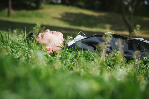 Asian teenage girl wearing school uniform lying down on grass and listening to music.