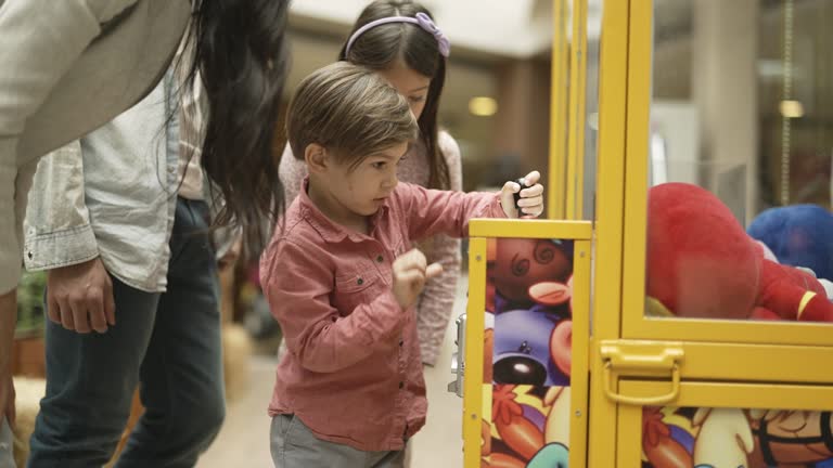 Little boy putting some coins provided by mother into toy grabbing machine