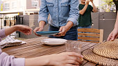 Group of man woman asia people fun joy prepare set dine table plate glass cutlery in cozy party host event at home front yard patio. Young adult child friend enjoy happy warm time picnic lunch meal.