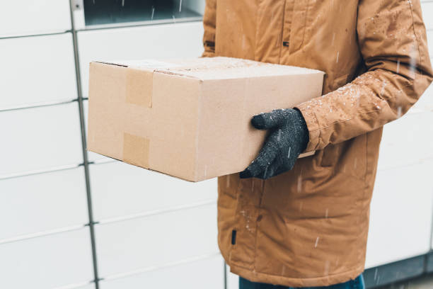 istock A man with a box in his hands near the self-service mail terminal. Parcel delivery machine. Person holding a cardboard box. Mail delivery and post service, online shopping, e commerce concept 1475682228