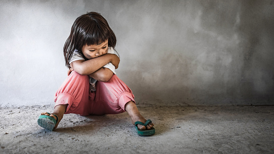 Sad little child girl sitting alone on floor concrete wall background