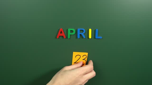 Hand sticking a sticker 23 April calendar day on school board. 23 date of April. Twenty third day of April. 23th date number. 23 day calendar. Twenty three date. National Sovereignty and Childrens