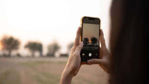 Asian woman using mobile phone to capture rising sun.