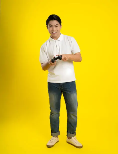 Portrait of young asianman playing game  on yellow background