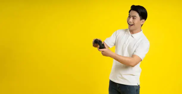 Portrait of young asianman playing game  on yellow background