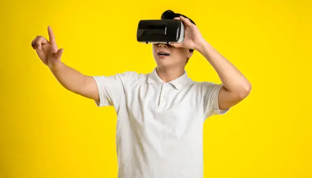 Portrait of young asianman play ing virtual reality on yellow  background